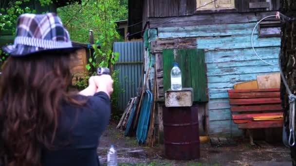 Het meisje in de hoed schiet een pistool en schiet een fles water - Video