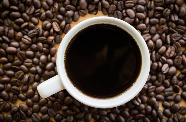Flat lay view of Black coffee in a white cup with coffee beans in background  - Photo, Image