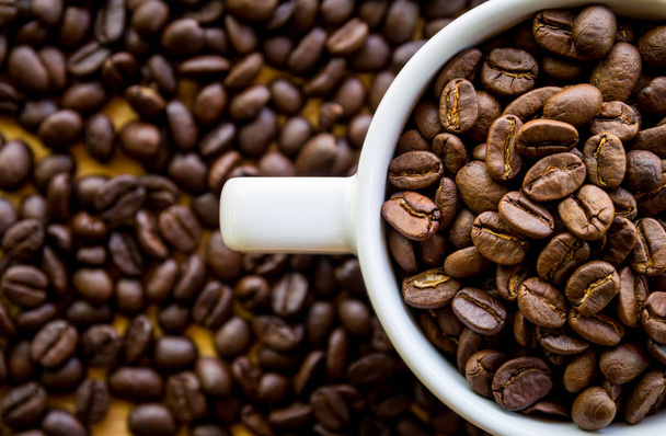 bílý šálek kávy plný kávových bobů, semen na povrchu stolu  - Fotografie, Obrázek