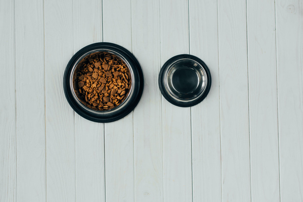 top view of bowl with pet food and empty bowl on wooden surface with copy space - Photo, Image