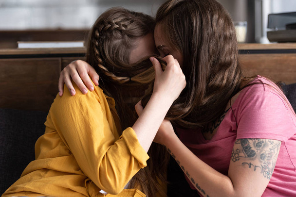 zwei Lesben bedecken Gesichter mit Haaren, während sie sich im Wohnzimmer umarmen und küssen - Foto, Bild