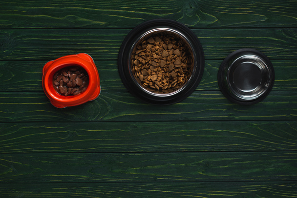 top view of bowls with pet food in row on green wooden surface - Foto, imagen