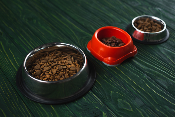 миски з кормом для домашніх тварин в ряд на зеленій дерев'яній поверхні
 - Фото, зображення