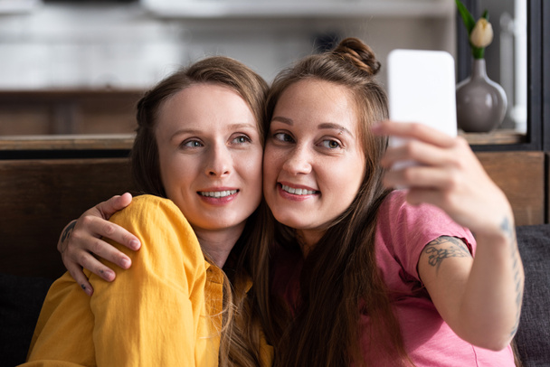 two lesbians embracing while taking selfie at home - Фото, изображение