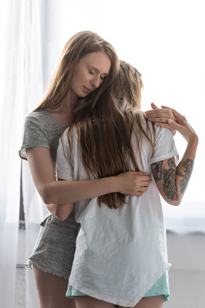 two smiling lesbians in t-shirts embracing in bedroom - Foto, Bild
