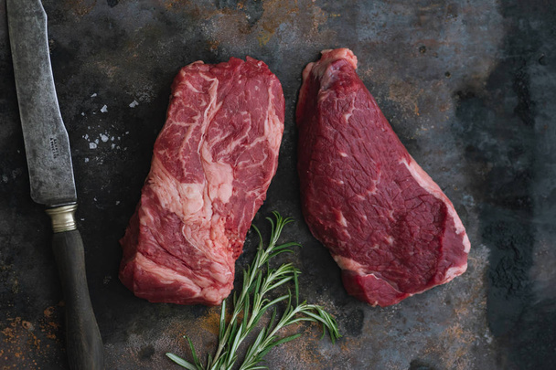 Raw black angus prime beef steaks with rosemary and sea salt with knife on dark background  - 写真・画像