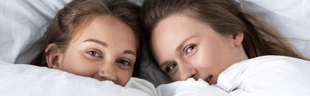 panoramische shot van twee lesbiennes liggend onder witte deken in de slaapkamer - Foto, afbeelding