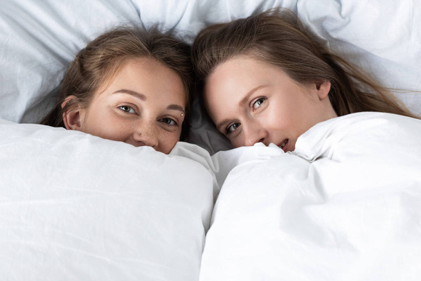 two lesbians lying under white blanket in bedroom - Photo, image