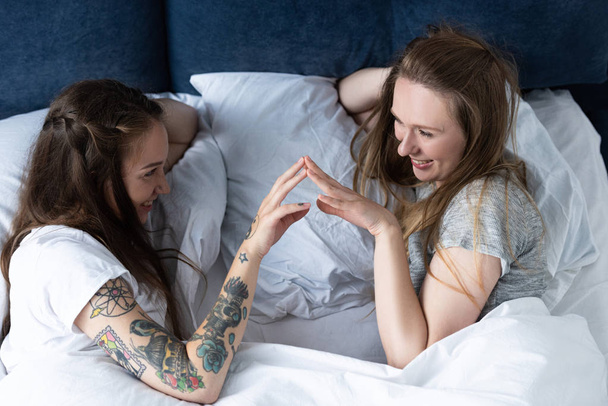 two smiling lesbians touching hands and looking at each other in bed - Фото, зображення