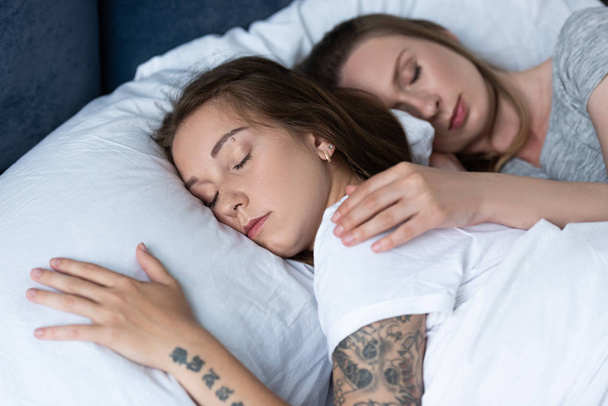 ベッドで毛布の下で寝ている間に抱きしめる2人のレズビアン - 写真・画像