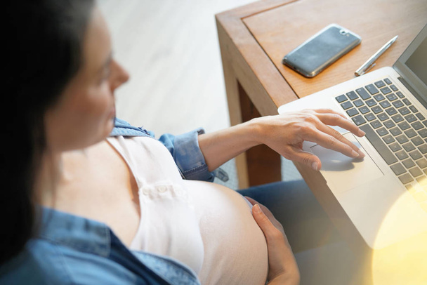 Closeup of pregnant woman belly and laptop in office - Foto, Imagem