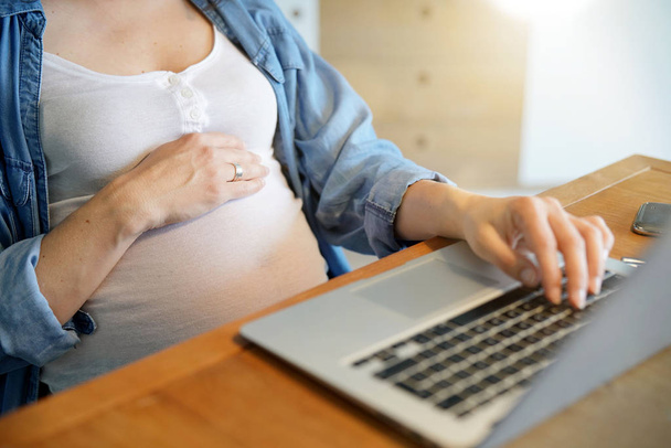 Closeup of pregnant woman belly and laptop in office - Foto, Imagen
