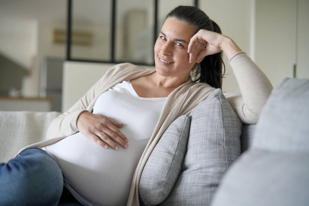 Portrait of pregnant woman relaxing in sofa - Foto, afbeelding