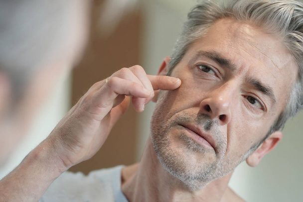Portrait of mature handsome man looking in mirror at home - Foto, afbeelding