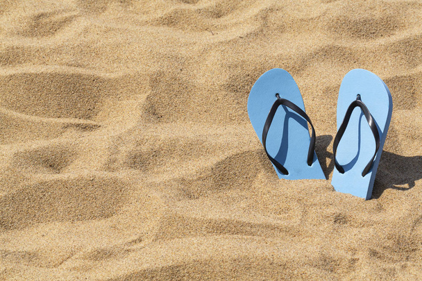 Kesällä tausta rannalla ja kengät hiekalla. Siniset sandaalit aurinkoisella trooppisella rannalla
. - Valokuva, kuva
