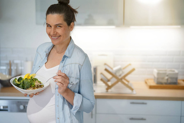 Pregnant woman in home kitchen eating healthy salad - Фото, изображение