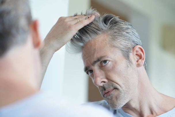 Portrait of mature handsome man looking in mirror at home - Foto, imagen