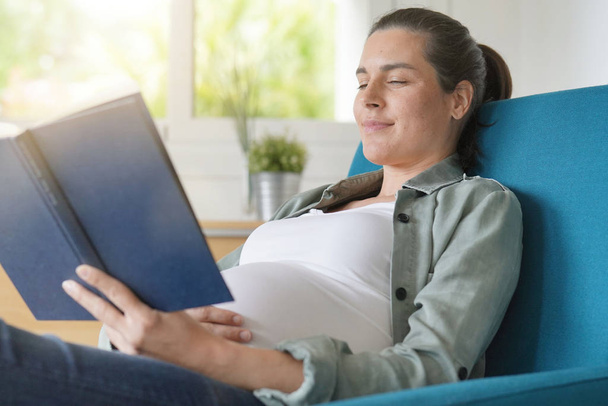 Femme enceinte dans un fauteuil lire un livre et se détendre
 - Photo, image