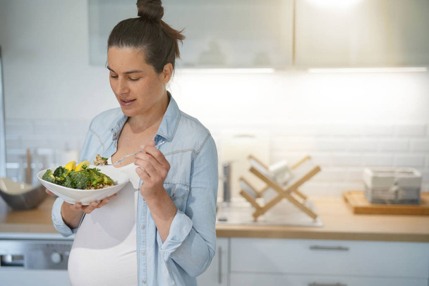 Pregnant woman in home kitchen eating healthy salad - Foto, afbeelding