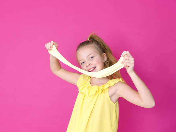 beautiful little girl playing with yellow slime in front of pink background - Fotoğraf, Görsel