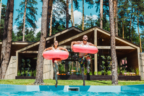 cheerful man and woman with inflatable rings jumping in swimming pool  - Photo, Image