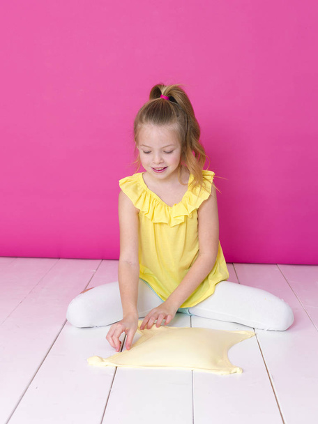 beautiful little girl playing with yellow slime in front of pink background - Фото, зображення