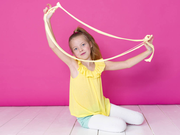 beautiful little girl playing with yellow slime in front of pink background - Фото, изображение