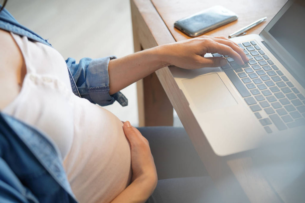 オフィスで妊娠中の女性の腹とラップトップのクローズアップ - 写真・画像