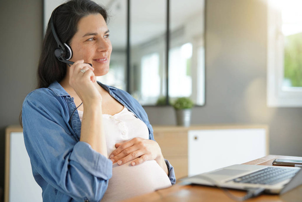 Pregnant woman working from home with laptop and headset - Photo, Image
