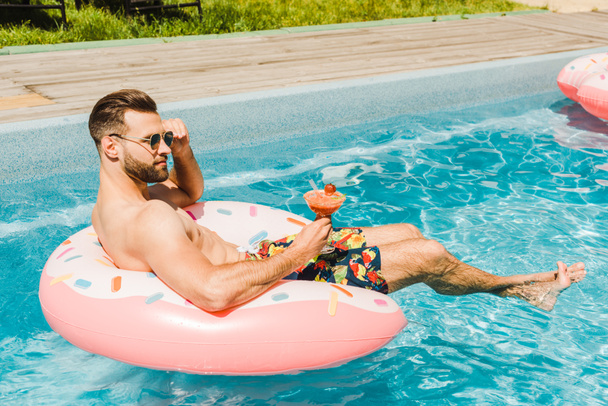 hombre guapo tocando gafas de sol y sosteniendo copa de cóctel
  - Foto, imagen