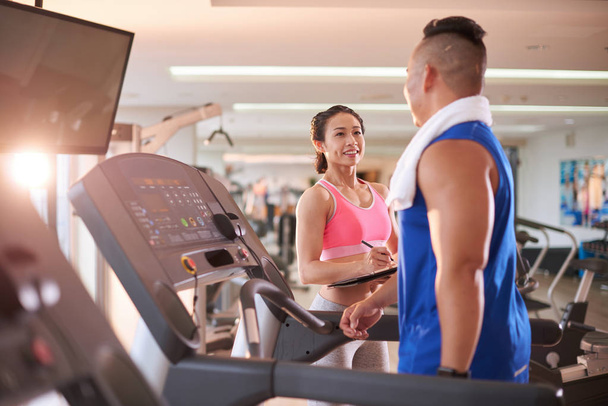 Pretty fitness trainer taking notes when talking to client in gym - 写真・画像