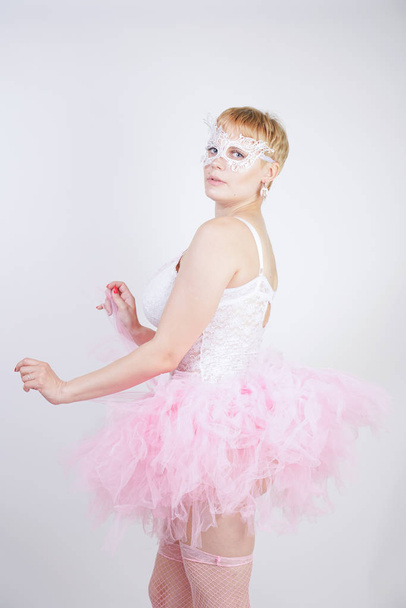 pretty plus size playful adult girl in white lace corset and tutu skirt standing alone on studio background. cute blonde chubby woman in pink dress posing as a doll. - Foto, Imagem