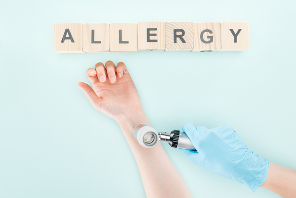 обрізаний вид лікаря, який вивчає руку жінки з дерматоскопом біля дерев'яних блоків зі словом алергія ізольовано на синьому
 - Фото, зображення