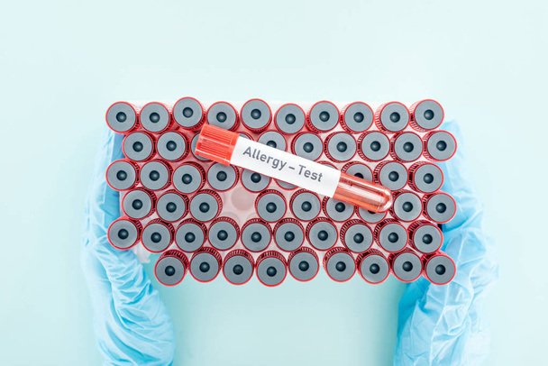cropped view of doctor in latex gloves holding test tubes with sample above other tubes on blue - Fotografie, Obrázek