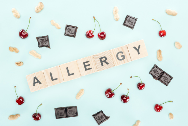 top view of wooden blocks with allergy lettering near cherries, nuts and chocolate isolated on blue - Photo, Image