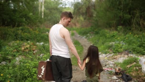 Hajléktalan apa és lánya távolodik végig az erdei ösvényen keresztül a szemétlerakó. A környezetszennyezés, a szegénység és a hajléktalanság fogalma. - Felvétel, videó