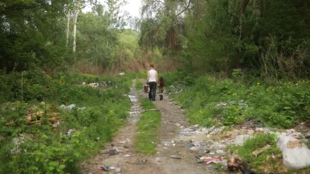 Безпритульні батько і дочка рухаються лісовою дорогою через сміттєзвалище. Концепція забруднення навколишнього середовища, бідності та безпритульності
. - Кадри, відео