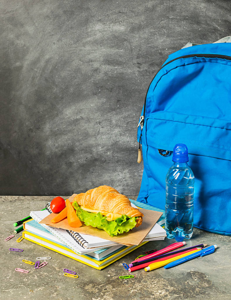 Sandwich training supplies notebooks blauwe rugzak tegen de achtergrond van het krijtbord. Concept terug naar school. - Foto, afbeelding