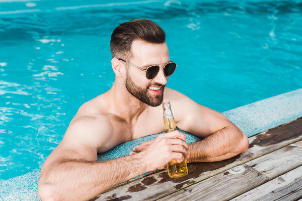 весёлый бородатый мужчина в солнечных очках держит бутылку с пивом
  - Фото, изображение