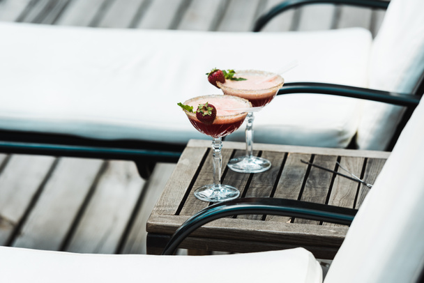 selective focus of cocktail glasses with drinks on wooden table near deck chairs  - Foto, imagen