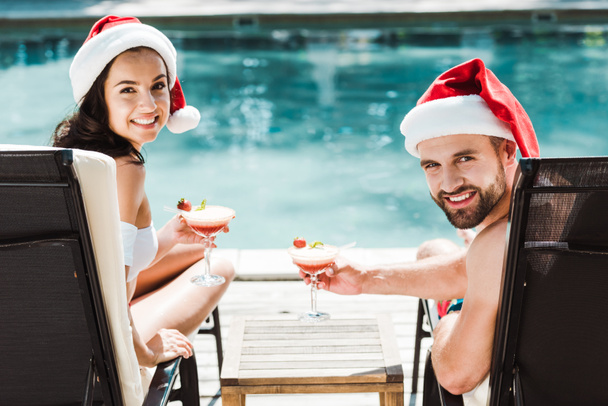 Gelukkige vrouw en man in Sants Claus hoeden houden cocktail glazen  - Foto, afbeelding