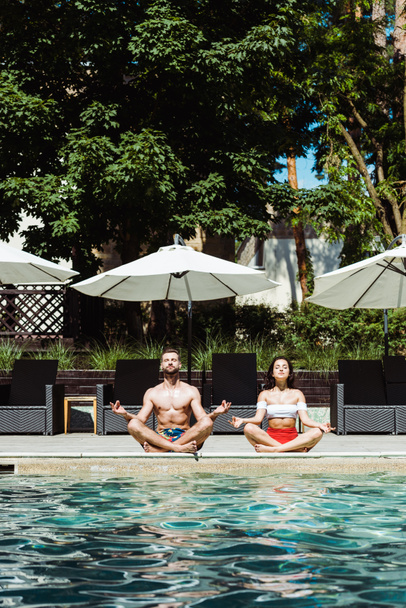 attractive woman and handsome man meditating near swimming pool   - Фото, изображение