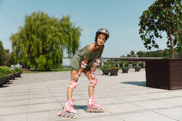 Teenage girl in a helmet learns to ride on roller skates outdoors - Foto, Imagen