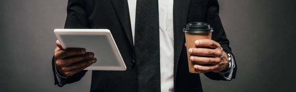 vue partielle de l'homme d'affaires afro-américain tenant du café à emporter et tablette numérique sur fond sombre, panoramique
 - Photo, image