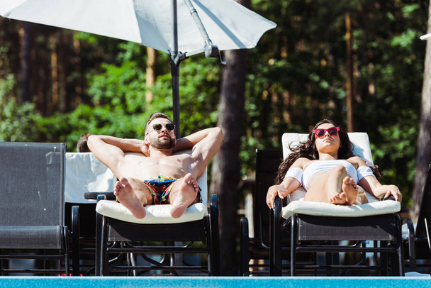 handsome man and beautiful woman in sunglasses lying on deck chairs  - Photo, Image