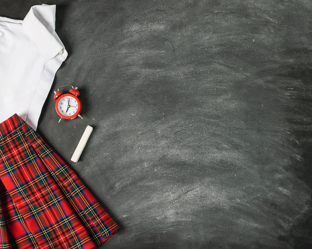 Escuela uniforme camisa blanca falda a cuadros reloj despertador el fondo de pizarra. Concepto de regreso a la escuela y la educación
. - Foto, Imagen