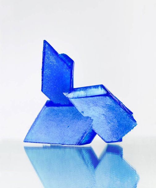 Μπλε κρύσταλλοι θειικού χαλκού στην επιφάνεια του καθρέφτη, λευκό φόντο, μπλε βιόλη, θειικό χαλκό - Φωτογραφία, εικόνα