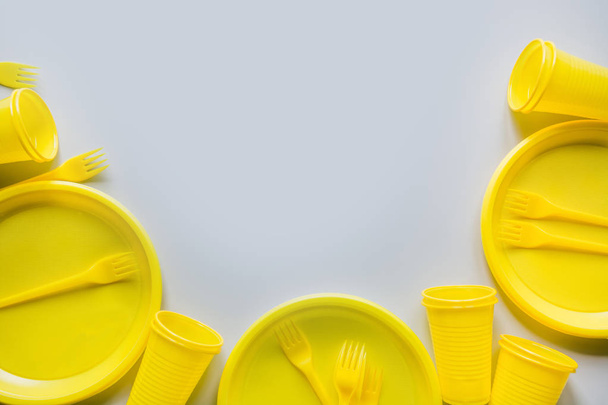 Single use picnic yellow utensils, plates, cups, forks on grey. Top view. Space for text. - 写真・画像