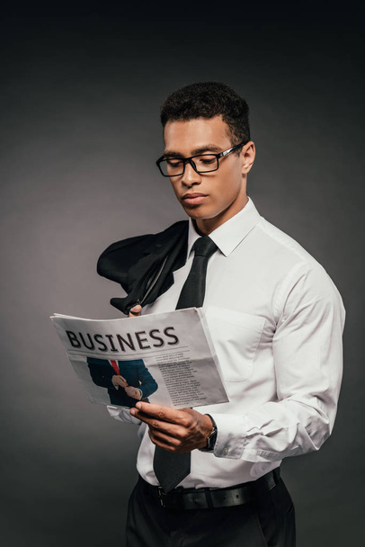 african american businessman holding blazer and reading newspaper on dark background - 写真・画像