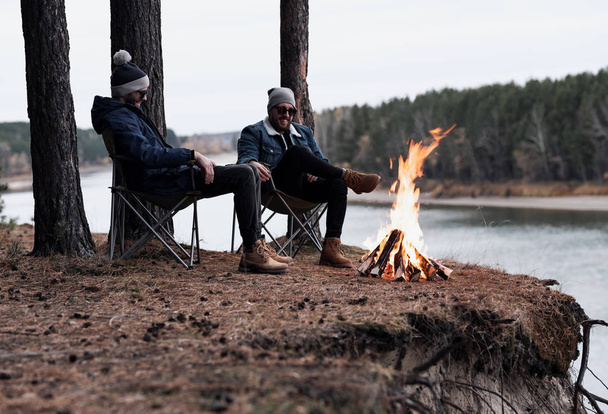 Male friends resting around bonfire by river - Foto, imagen